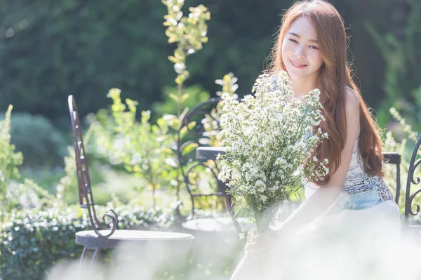 Ásia jovem mulher com flores sentado na cadeira no parque — Fotografia de Stock