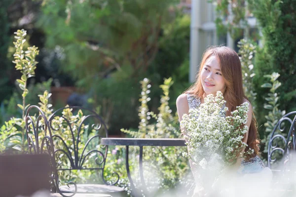 Asia giovane donna con fiori seduta sulla sedia nel parco — Foto Stock