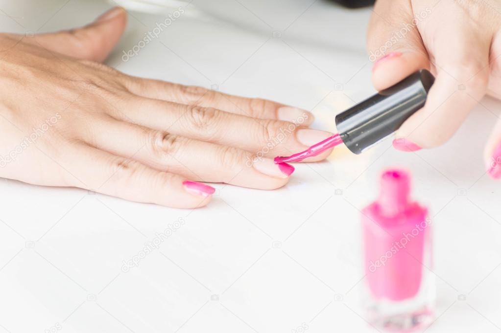 Woman applying pink nail polish on hand