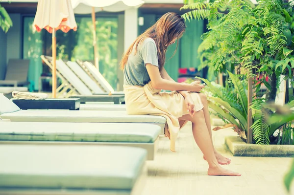 Hermosa mujer usando el teléfono inteligente en la tumbona cerca de la piscina — Foto de Stock