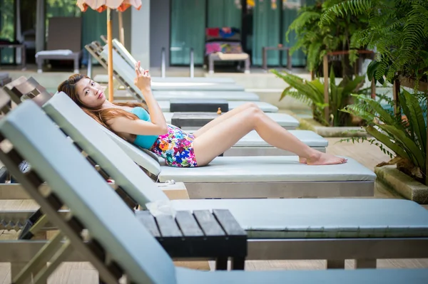 Mulher bonita usando telefone inteligente na espreguiçadeira perto da piscina — Fotografia de Stock