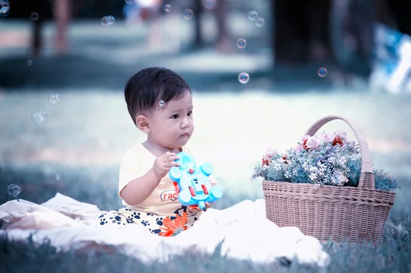 Азія хлопчика, сидячи на зеленій траві з мильними бульбашками — стокове фото