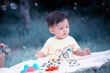 Sabun köpüğü ile yeşil çimenlerin üzerinde oturan erkek Asya bebek 