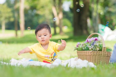 Sabun köpüğü ile yeşil çimenlerin üzerinde oturan erkek Asya bebek 