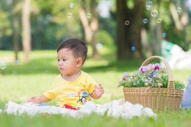 Sabun köpüğü ile yeşil çimenlerin üzerinde oturan erkek Asya bebek 