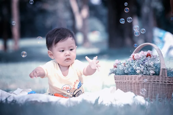 Sabun köpüğü ile yeşil çimenlerin üzerinde oturan erkek Asya bebek 