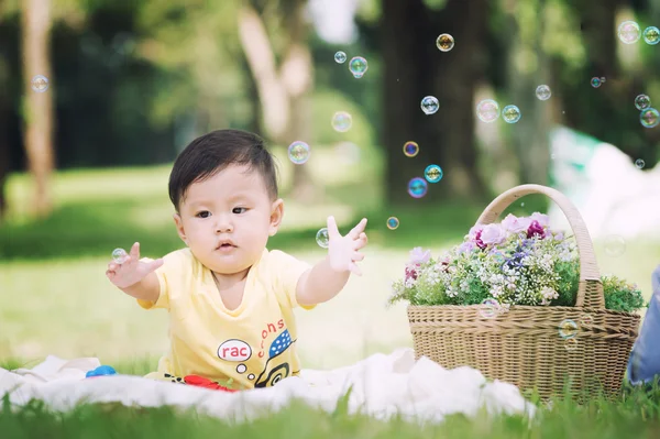 Asia Niño sentado sobre hierba verde con burbujas de jabón — Foto de Stock