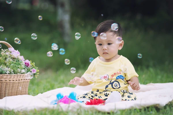 Азиатский мальчик сидит на зеленой траве с мыльными пузырями — стоковое фото