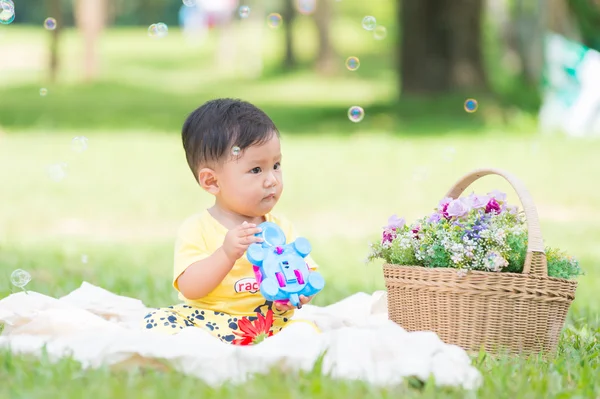 Азиатский мальчик сидит на зеленой траве с мыльными пузырями — стоковое фото