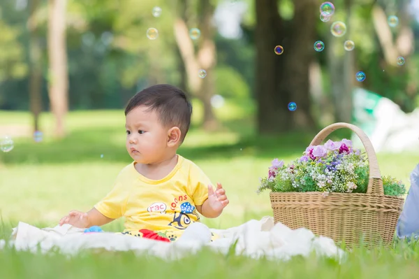 Sabun köpüğü ile yeşil çimenlerin üzerinde oturan erkek Asya bebek 