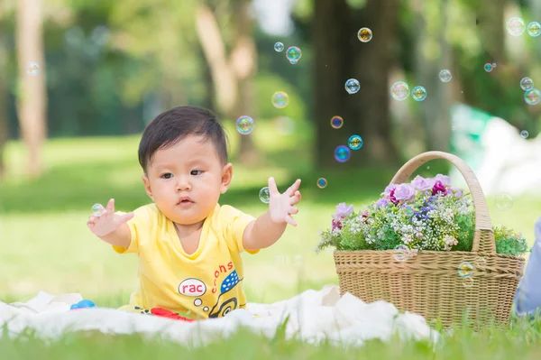 Ásia Menino sentado na grama verde com bolhas de sabão — Fotografia de Stock