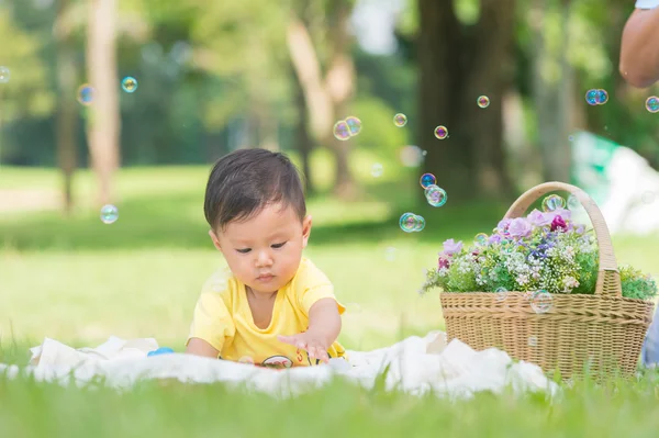 Sabun köpüğü ile yeşil çimenlerin üzerinde oturan erkek Asya bebek 