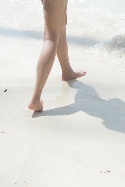 Kumsalda yürüyen bir kadın kumların üzerinde ayak izleri bırakıyor.