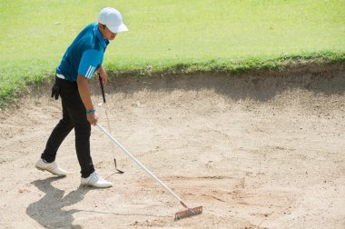 golfer racking sand at golf course, thailand clipart