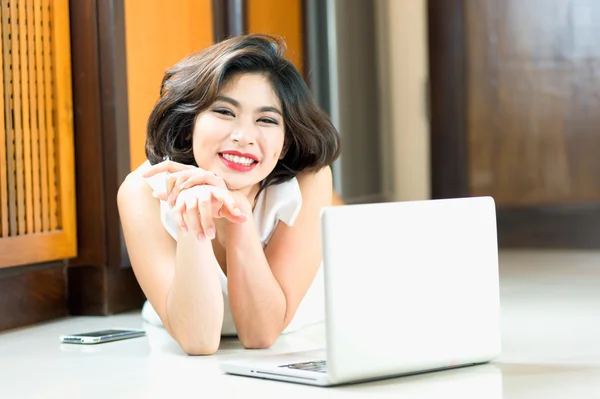 Mujer asiática feliz acostada en el suelo con el ordenador portátil en casa — Foto de Stock