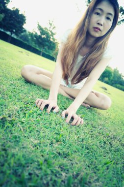Asya güzel genç kadın oturur Park, el çimenlerin üzerinde