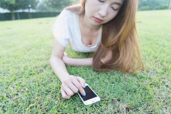 Asia women write text messaging on her phone lying on grass — Stock Photo, Image