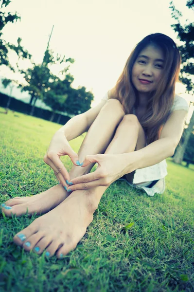 Azji kobieta siedzi na trawie co serce — Zdjęcie stockowe