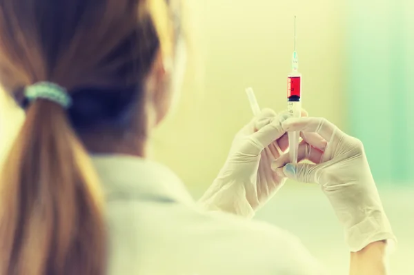 Médico con jeringa de vacuna roja en la mano —  Fotos de Stock