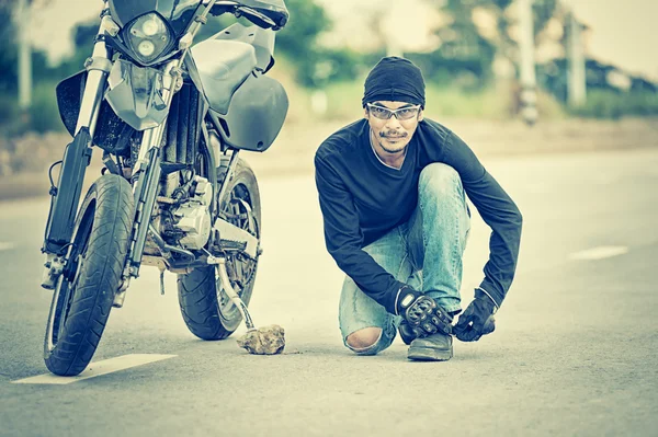 Moto garée dans la route de campagne avec le motard attachant ses chaussures — Photo