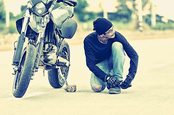 Motocicleta estacionada en la carretera del campo con Biker atando sus zapatos — Foto de Stock