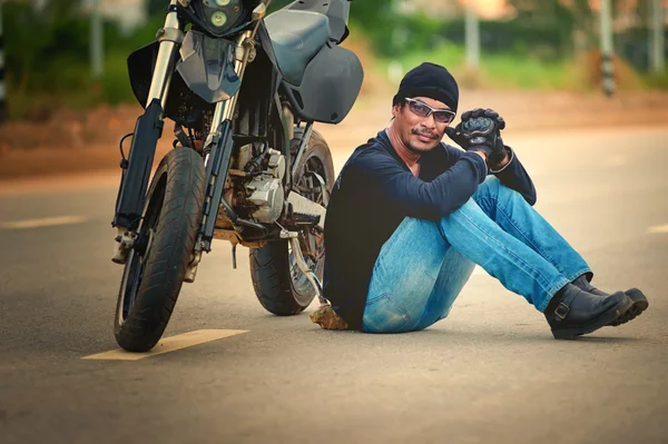 Motociclista relajarse sentado con la moto en la carretera en la puesta del sol — Foto de Stock