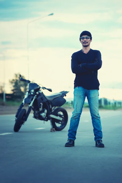 Портрет чоловіка-байкера, що стоїть на дорозі з мотоциклом — стокове фото