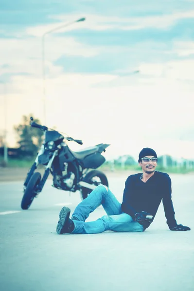 Biker relaxar sentado com moto na estrada ao pôr do sol — Fotografia de Stock