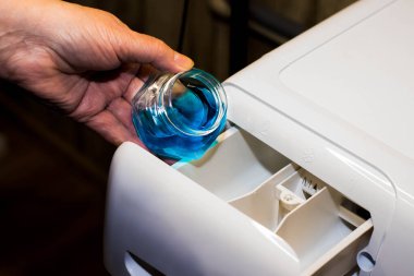 Çamaşır makinesine mavi renkli sıvı çamaşır tozu dökülüyor.