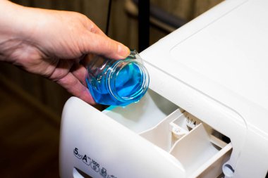 Çamaşır makinesine mavi renkli sıvı çamaşır tozu dökülüyor.