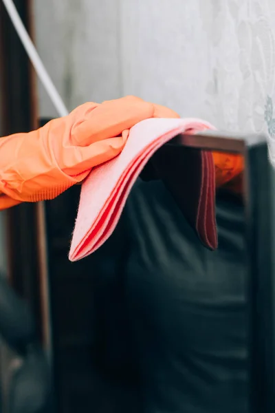 the woman tidies the room by dusting the TV with a gloved rag