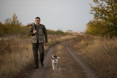 Hunter with Russian spaniel dog walking on the dirt road. Image taken during big game hunting trip. Hunting period, autumn season open. clipart