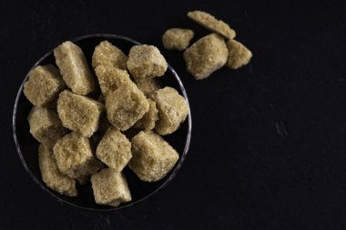 Çelik kasede koyu arkaplanda doğal kahverengi şeker küpleri. Üst görünüm.