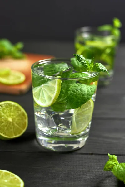 İki bardak limonata ya da buzlu mojito kokteyli, taze nane ve limon. Siyah masada soğuk, ferahlatıcı bir kokteyl.