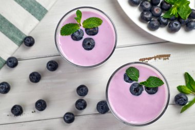 Beyaz ahşap bir masada taze yaban mersini ve nane yapraklarıyla servis edilen yaban mersinli yoğurt. Sağlıklı kahvaltı. Üst görünüm.