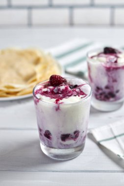 Vanilyalı dondurma ve böğürtlen soslu lezzetli tatlı ve arka planda iştah açıcı krepler.