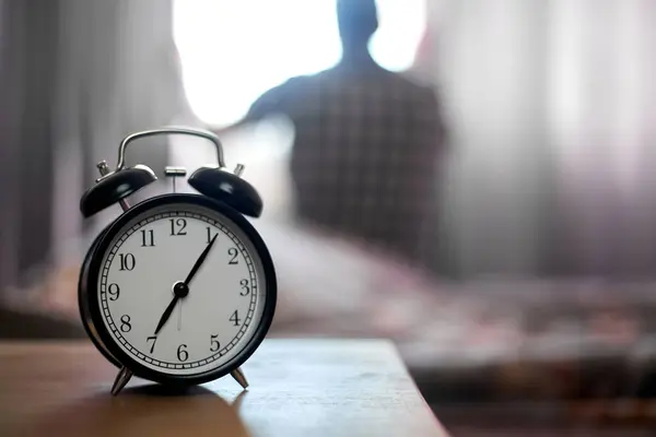 Yatak odasında çalar saat ve uyandıktan sonra genç bir adam, sabah güneş ışığı..