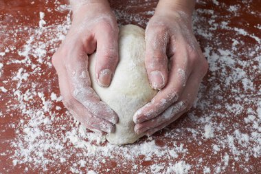 Kadın elleriyle hamuru yoğuruyor. Ahşap bir arka planda kadın eli ve ham hamur. Pizza hamuru ya da pişmiş mal. Ekmek, pizza, makarna..