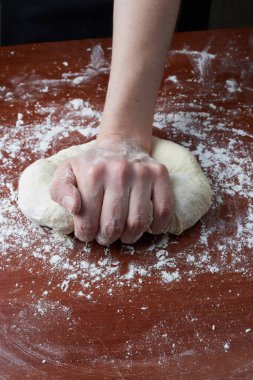 Kadın elleriyle hamuru yoğuruyor. Ahşap bir arka planda kadın eli ve ham hamur. Pizza hamuru ya da pişmiş mal. Ekmek, pizza, makarna..