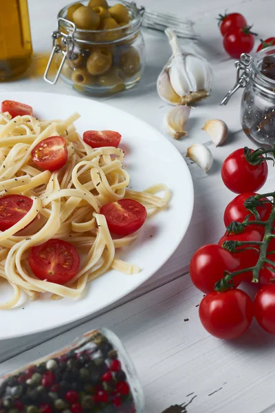 Kiraz domatesli lezzetli tagliatelle makarnası ve ahşap bir tabakta fesleğen ile birlikte makarna malzemeleri: zeytin, domates, sarımsak, zeytinyağı ve farklı türde kurutulmuş biber..