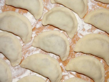 Ev yapımı hamur köfteleri un tozuyla kaplanmış ahşap bir masanın üzerinde duruyor. Üst görünüm.