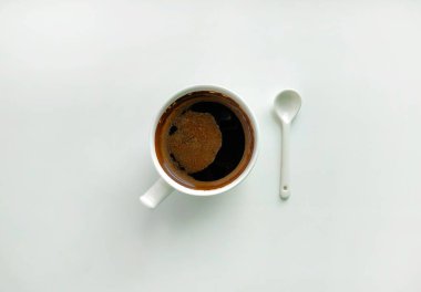Beyaz arka planda beyaz bir fincan kahve ve beyaz seramik kaşık. Üst açı 