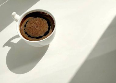 Beyaz arka planda sert gölgeli beyaz bir fincan kahve.