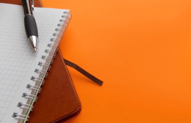 Kahverengi defter, beyaz bahar defteri ve parlak turuncu arka planda siyah kalem.