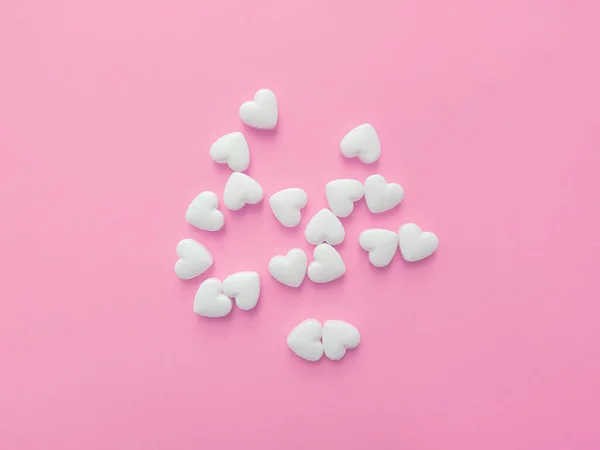 White pills in the shape of hearts on a pastel pink background