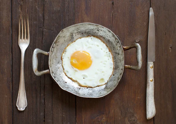 Жареное яйцо в старой сковороде с вилкой и ножом — стоковое фото