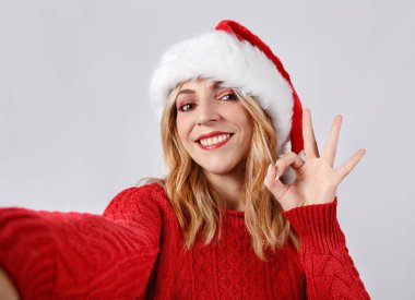 Noel Baba şapkalı genç bir kadın selfie çekiyor ve parmakları griden izole bir şekilde işaret veriyor.