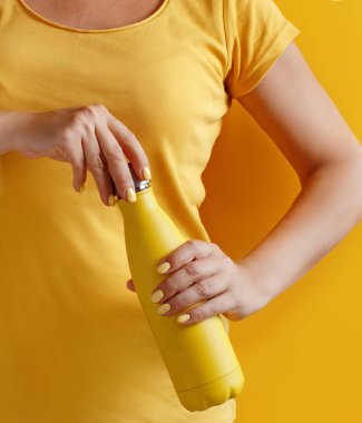 Sarı arka planda sarıyı tekrar kullanılabilir şişeyi tutan kadına yaklaş.