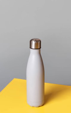 Gri ve sarı arka planda gri yeniden kullanılabilir çelik şişe yakın plan. Sıfır atık, plastiksiz ve sürdürülebilir yaşam tarzı kavramı