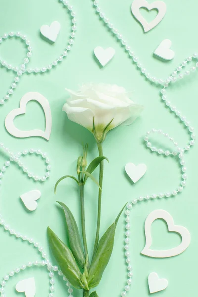 White flower with pearls and hearts around on a light green background  top view